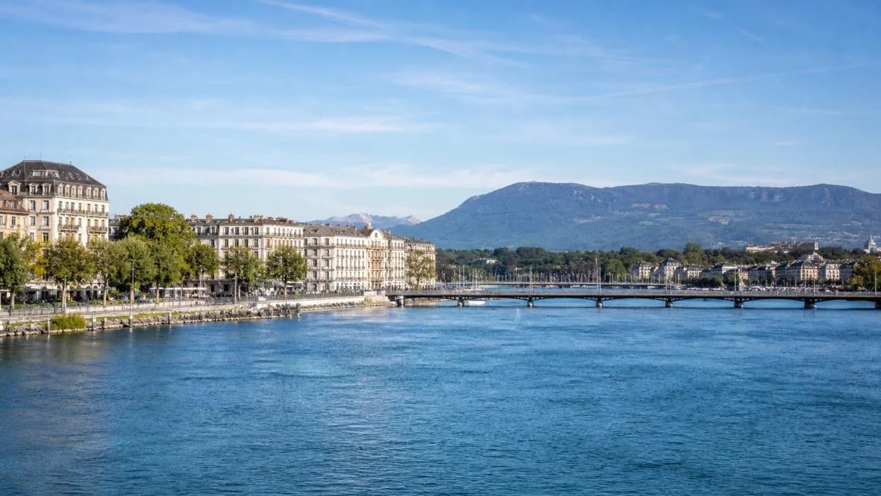 Lakeside buildings and a bridge in Switzerland, with mountains beyond.